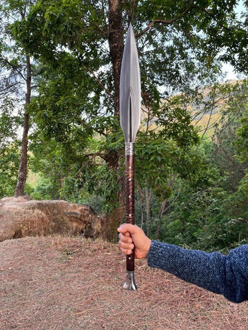 Person holding a large viking spear outdoors with trees in the background